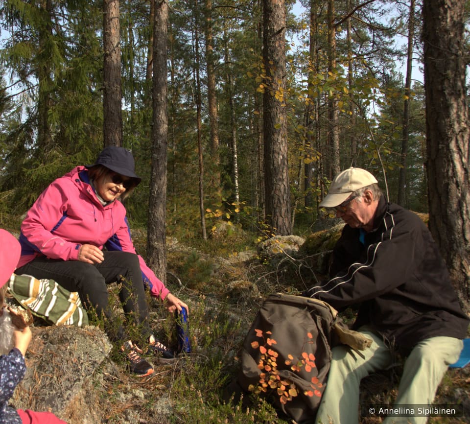 An elderly couple sitting on the forest floor having a relaxed coffee and snacks.