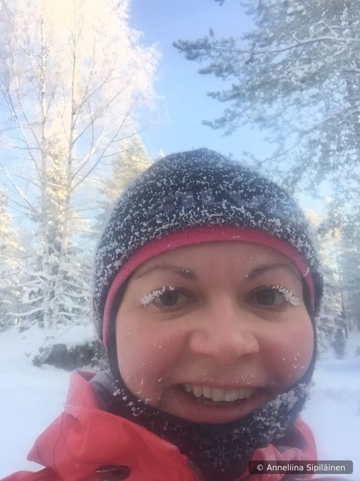 Guide smiling with frosty eyelashes, surrounded by snow-laden spruce trees.