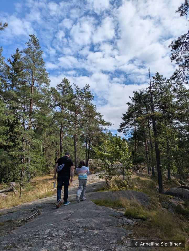 A man and a girls walking on bed rock cliff on a sun lit forest path